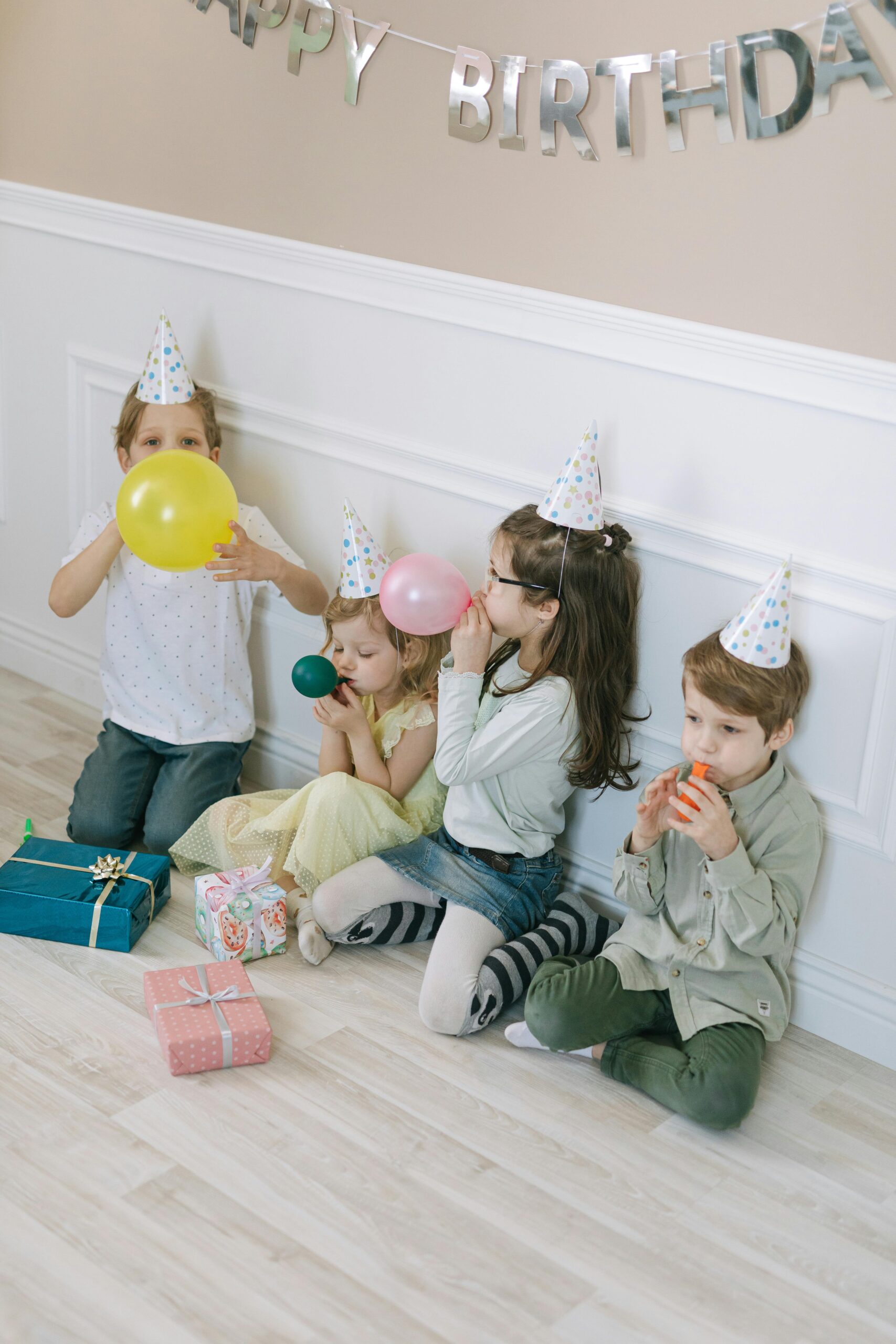 Group of children celebrating a birthday party indoors with balloons and gifts.